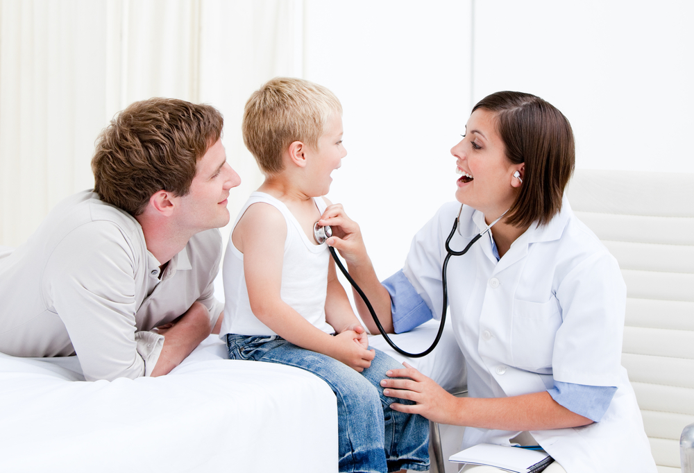 Beautiful female doctor examining a little boy with his father at the hospital