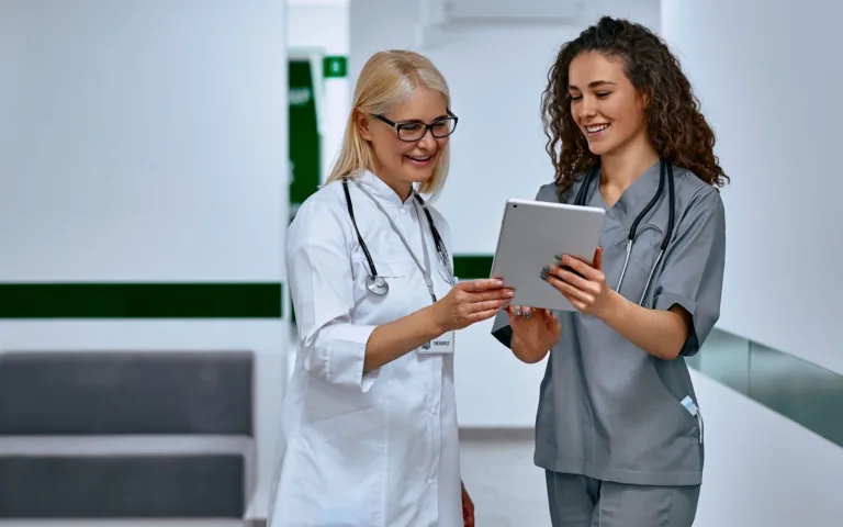 Two women in scrubs are looking at a tablet