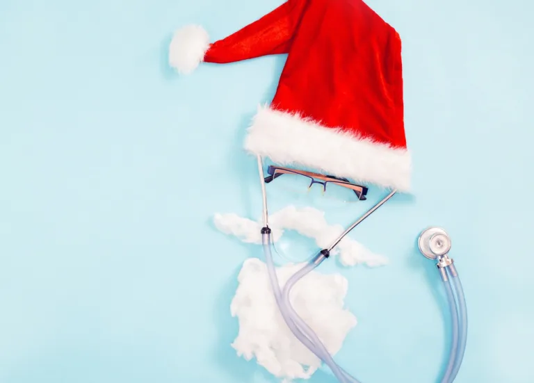 The concept of a doctor in a santa claus hat with a beard in glasses with a stethoscope on a blue background. copy space. Flat lay. Health and medicine banner for Christmas, happy new year