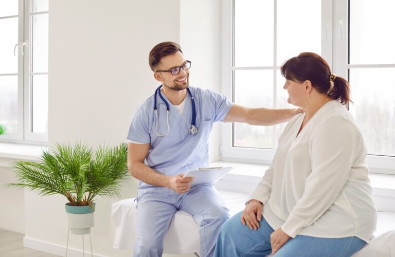 Overweight woman having consultation at the office. Portrait of friendly smiling doctor putting hand on shoulder supporting patient, giving consultation during medical examination in clinic.