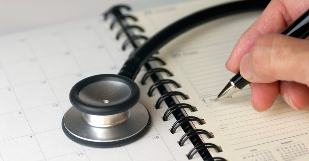Doctor writing a summer hospital staff schedule in a planner with a stethoscope, illustrating flexible scheduling strategies for healthcare staffing.