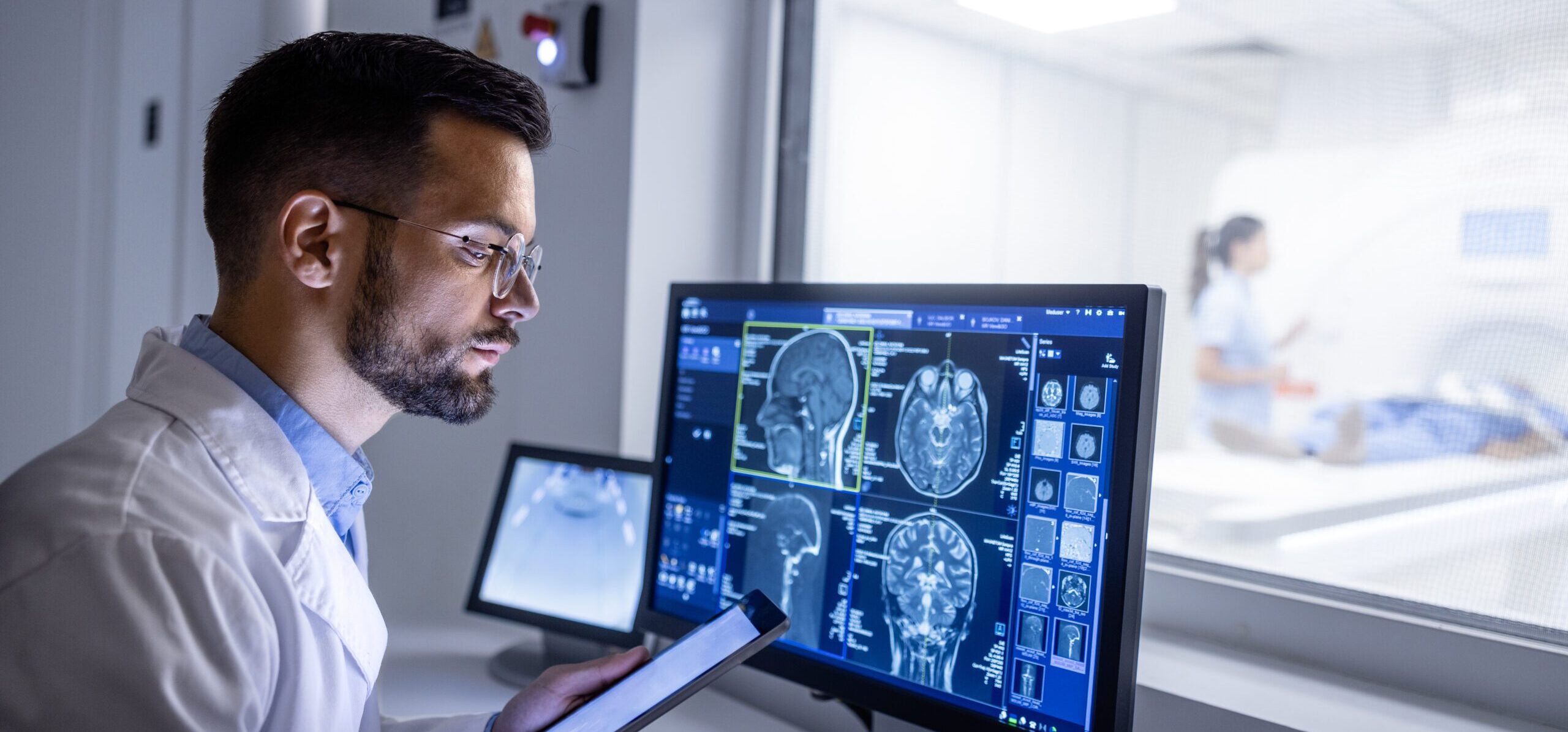 A doctor in a room is examining medical imaging, such as an X-ray or MRI, on a computer monitor.