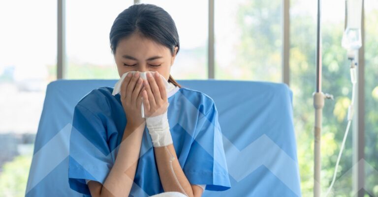 female flu season patient in a hospital bed blowing her nose into tissue