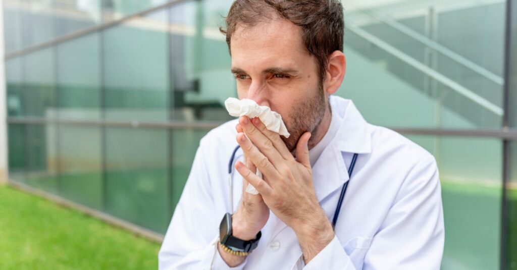 male physician sick during flu season blowing nose outside hospital